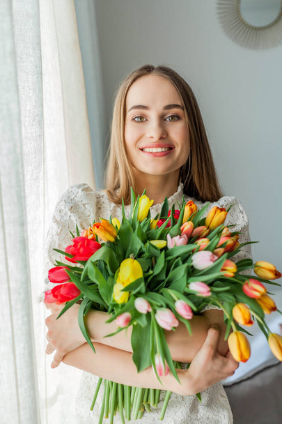 Hermosa mujer joven sostiene un ramo multicolor de tulipanes. Retrato mujer primavera
. - Foto, imagen