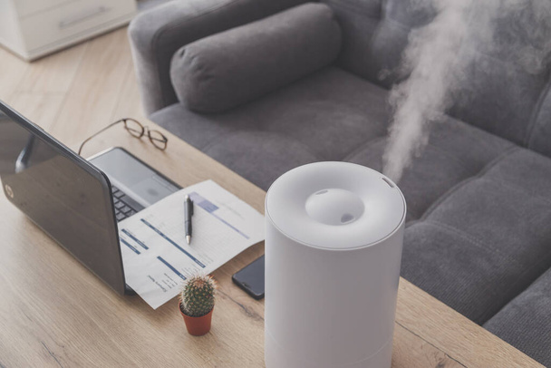 Household humidifier in the workplace to maintain relative humidity and microclimate in the workplace of the home office with a laptop and documents - Photo, Image