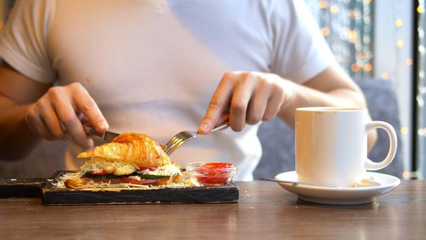 closeup. man eating a croissant with bacon and coffee in a cafe - Foto, Bild