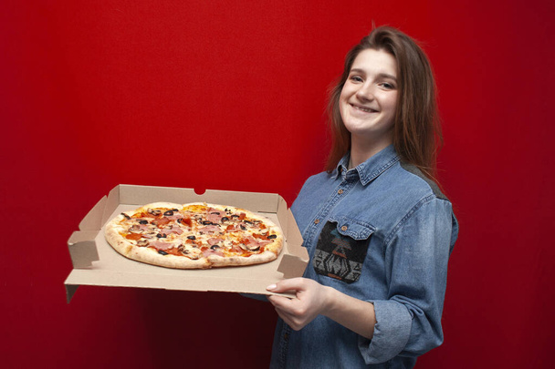 fiatal boldog lány tart egy nagy pizza egy dobozban egy színes piros háttér, egy diák nyit egy friss pizza, másolás helyet - Fotó, kép