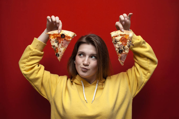 面白い若い驚きの女の子は、色の背景においしいピザの2つのスライスを保持しています,ティーンエイジャーは、ファーストフードを食べるのが好き,隔離された - 写真・画像