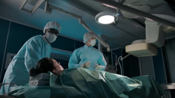 Ein dunkelhäutiger Arzt bewegt einen Operationstisch mit einer kaukasischen Patientin - Filmmaterial, Video