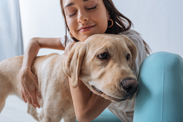 Beautiful woman with closed eyes petting golden retriever isolated on grey - Foto, Bild