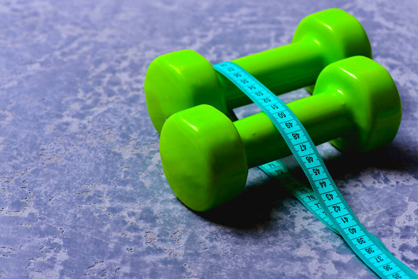 Dumbbells in green color and cyan measuring tape around them - Fotografie, Obrázek