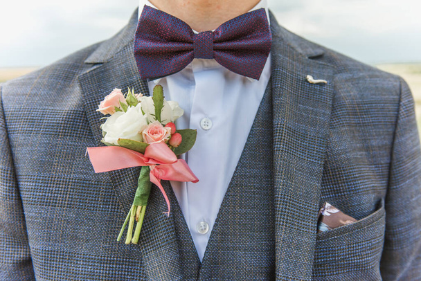 Un boutonniere blanco atado a la chaqueta de un novio con una mariposa. Preparándose para la boda. Cierre
 - Foto, imagen