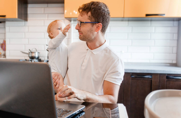 Handsome young man working at home with a laptop with a baby on his hands. Stay home concept. Home office with kids.  - Foto, imagen