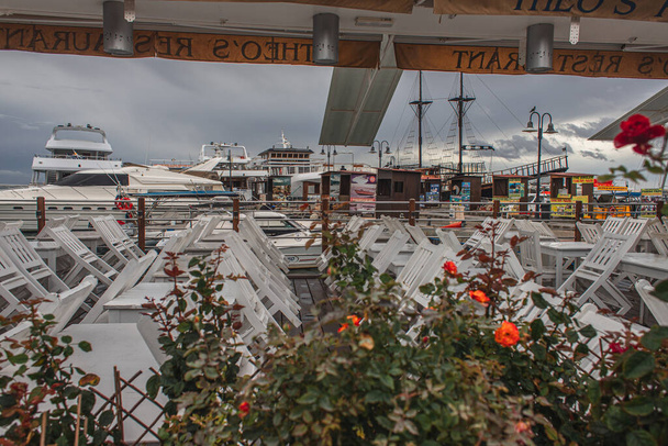 PAPHOS, CYPRUS - MARCH 31, 2020: green plants, tables and chairs on terrace near yacht club  - Фото, зображення
