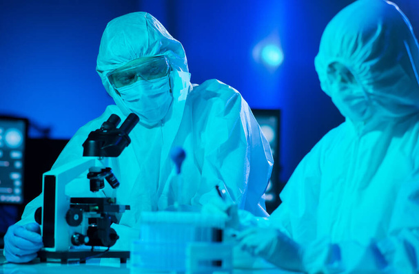 Scientists in protection suits and masks working in research lab using laboratory equipment: microscopes, test tubes. Medicine, coronavirus 2019-ncov infection and vaccine discovery concept. - Foto, imagen