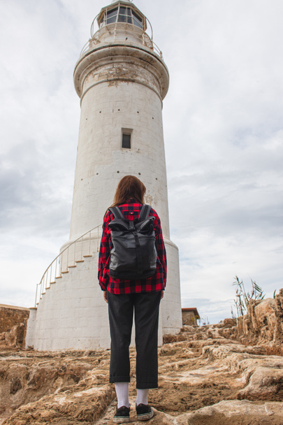 back view of traveler with backpack standing near white lighthouse - Foto, afbeelding