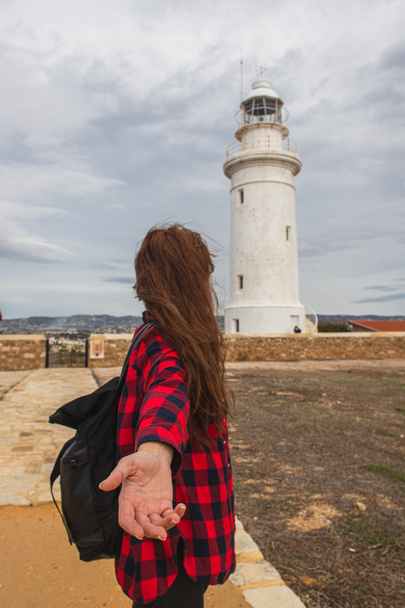 back view of woman with outstretched hand standing near white lighthouse  - Foto, Bild