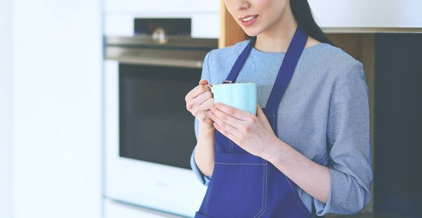 Portrait of young woman with cup against kitchen interior background - Foto, imagen
