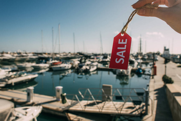vue recadrée de femme tenant étiquette rouge avec lettrage de vente près des yachts amarrés dans la mer Méditerranée
 - Photo, image