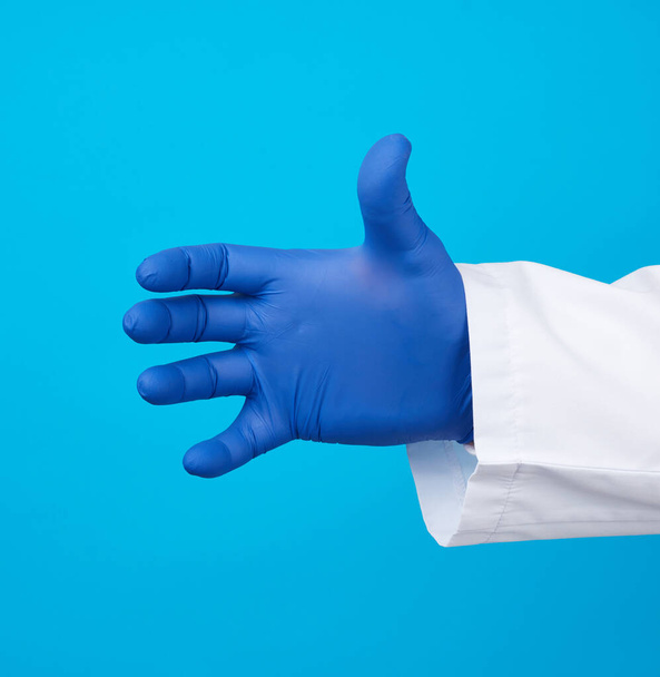  hand draagt een blauwe steriele rubberen handschoen met een voorwerp, blauwe achtergrond, element voor een ontwerper - Foto, afbeelding