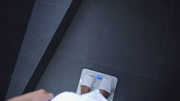 partial view of young woman walking and weighting on scales in bathroom - Imágenes, Vídeo