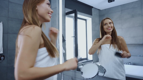 szczęśliwy młoda kobieta czesanie włosy przed lustrem w łazience - Materiał filmowy, wideo