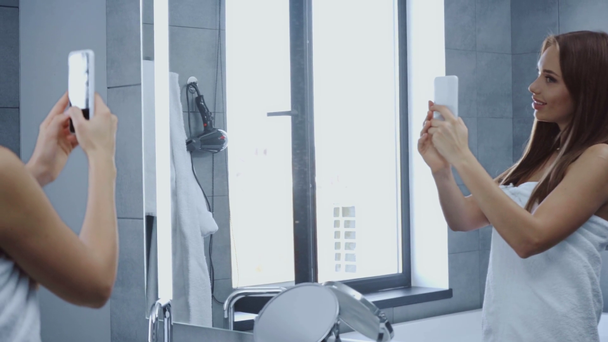 Banyodaki aynada selfie çeken banyo havlusu içinde güzel, mutlu genç bir kadın. - Video, Çekim