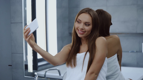 schöne junge Frau im Badetuch macht Selfie im Badezimmer - Filmmaterial, Video