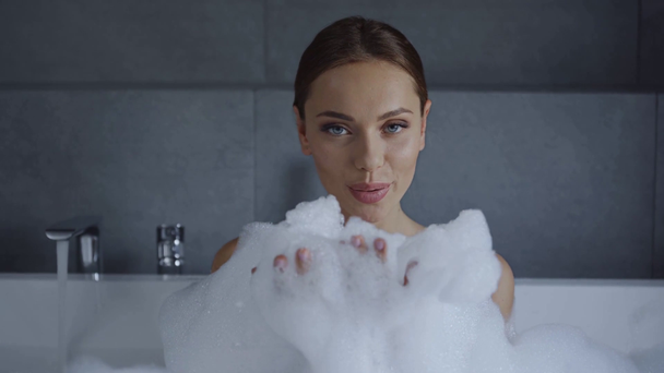 piękna młoda kobieta wieje na pianę mydlaną w kąpieli z bąbelkami - Materiał filmowy, wideo
