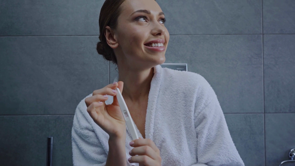jovem feliz olhando para o teste de gravidez positiva no banheiro
 - Filmagem, Vídeo