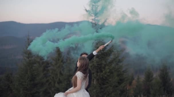 Newlyweds. Caucasian groom with bride on mountain slope with smoke bomb - Footage, Video