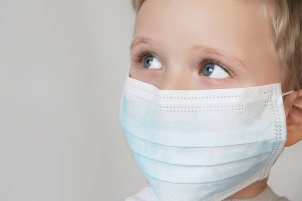 Παιδί με μπλε ιατρική μάσκα.Κοντινό πλάνο φωτογραφίας.Προστασία της υγείας από διάφορους ιούς και ασθένειες.Καραντίνα και πρόληψη ασθενειών έννοια. - Φωτογραφία, εικόνα