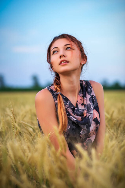 Schattig aantrekkelijk jong meisje op tarweveld bij zonsondergang. Pensieve blik. Romantische sfeer. - Foto, afbeelding