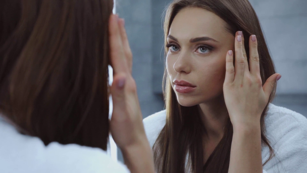 приваблива молода жінка торкається обличчя перед дзеркалом
 - Кадри, відео
