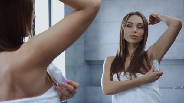 gyönyörű fiatal nő alkalmazása roll dezodor hónaljban a fürdőszobában - Felvétel, videó