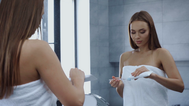 attractive young woman in bath towel preparing to brush teeth  - Materiaali, video