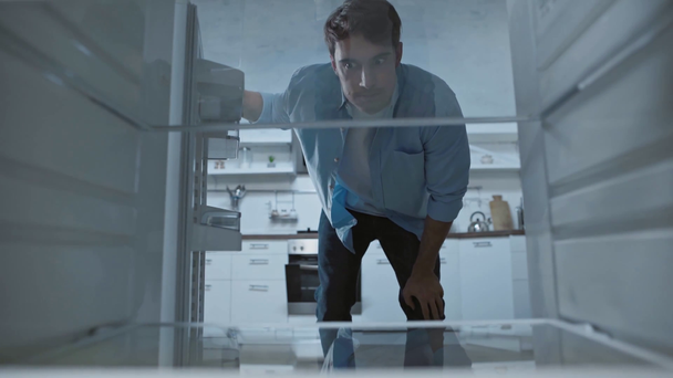 незадоволений чоловік дивиться в порожній холодильник на кухні
 - Кадри, відео