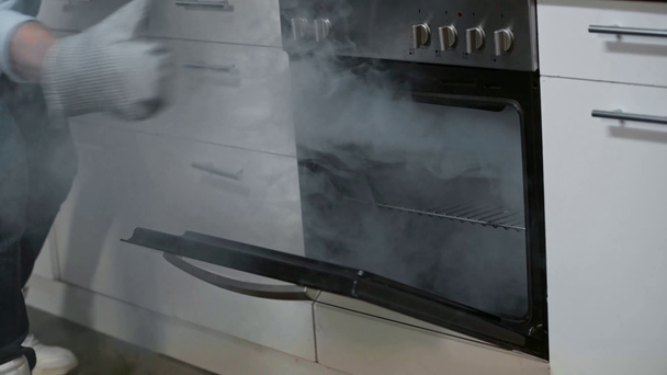 cropped view of man in kitchen gloves opening smoking oven in kitchen - Footage, Video