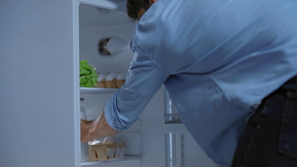 junger Mann öffnet Kühlschrank und nimmt Flasche mit frischer Milch - Filmmaterial, Video