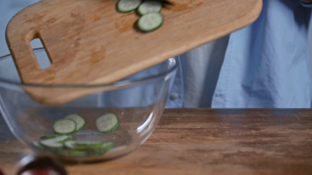 cropped view of man adding sliced cucumber into glass bowl - Felvétel, videó