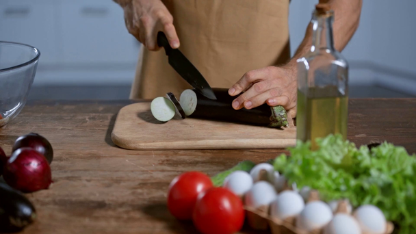 cropped view of man cutting eggplant near tomatoes, onion, chicken eggs and oil - Footage, Video
