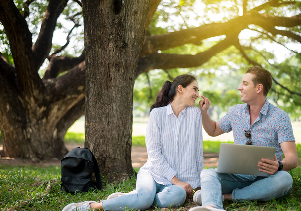 Genç aşıklar parkta oturup dizüstü bilgisayarlarını kullanıyorlar, romantik ve mutlu anlar geçiriyorlar, mutlu ve gülümsüyorlar. - Fotoğraf, Görsel