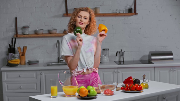 Chica sonriente sosteniendo pimentón mientras cocina ensalada en la cocina
  - Metraje, vídeo