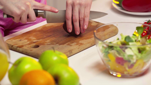 Vista recortada de la mujer cortando aguacate mientras cocina ensalada en la mesa
 - Imágenes, Vídeo