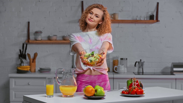 Smiling girl holding bowl with salad in kitchen  - Záběry, video