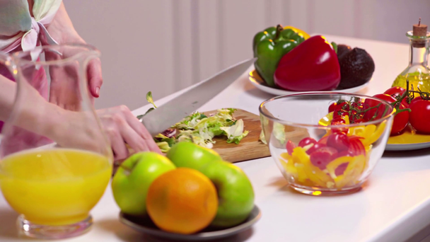 Vista ritagliata della donna che taglia lattuga vicino a frutta fresca e succo d'arancia sul tavolo
 - Filmati, video