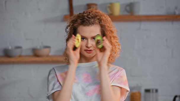 glimlachend meisje steken uit tong terwijl het houden van stukken van avocado  - Video
