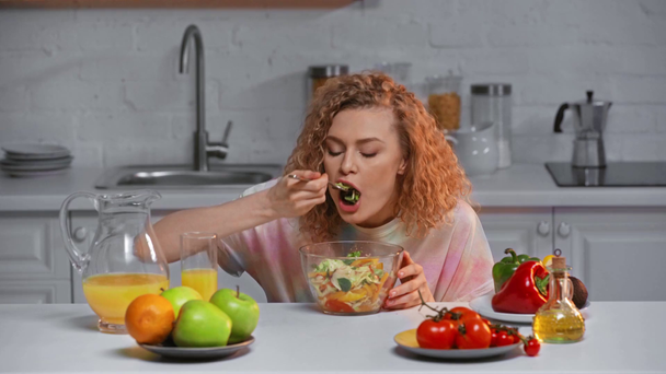 Fröhliche Frau isst frischen Salat am Küchentisch  - Filmmaterial, Video
