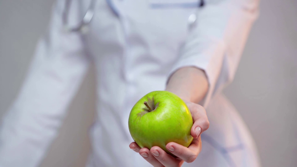 Selective focus of doctor holding green apple isolated on gray - Imágenes, Vídeo