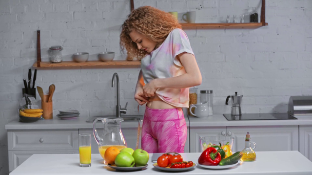 Traurige Frau misst Taille neben Obst und Gemüse auf Tisch - Filmmaterial, Video