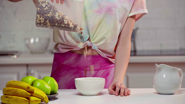 Vista recortada de la mujer vertiendo cereales en un tazón cerca de las frutas en la mesa
  - Imágenes, Vídeo