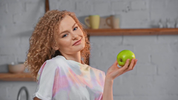 Chica sonriente sosteniendo manzana verde en la cocina
  - Imágenes, Vídeo