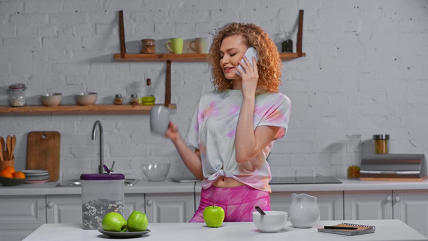 Mujer sonriente hablando en smartphone cerca de manzanas y cereales en la mesa
 - Metraje, vídeo