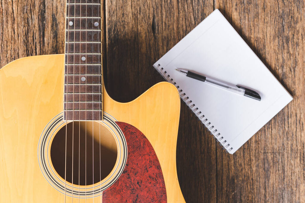 Вид зверху акустична гітара, папір для ноутбуків та ручка на фоні дерева та місце для тексту
 - Фото, зображення