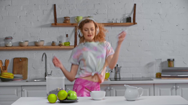 Kobieta w słuchawkach i smartphone taniec w pobliżu płatków śniadaniowych na stole - Materiał filmowy, wideo