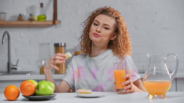 Hymyilevä nainen syö donitsia ja juo appelsiinimehua keittiössä
  - Materiaali, video