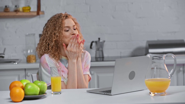 Mädchen mit Orangensaft weht Kuss, während sie Video-Chat auf Laptop - Filmmaterial, Video